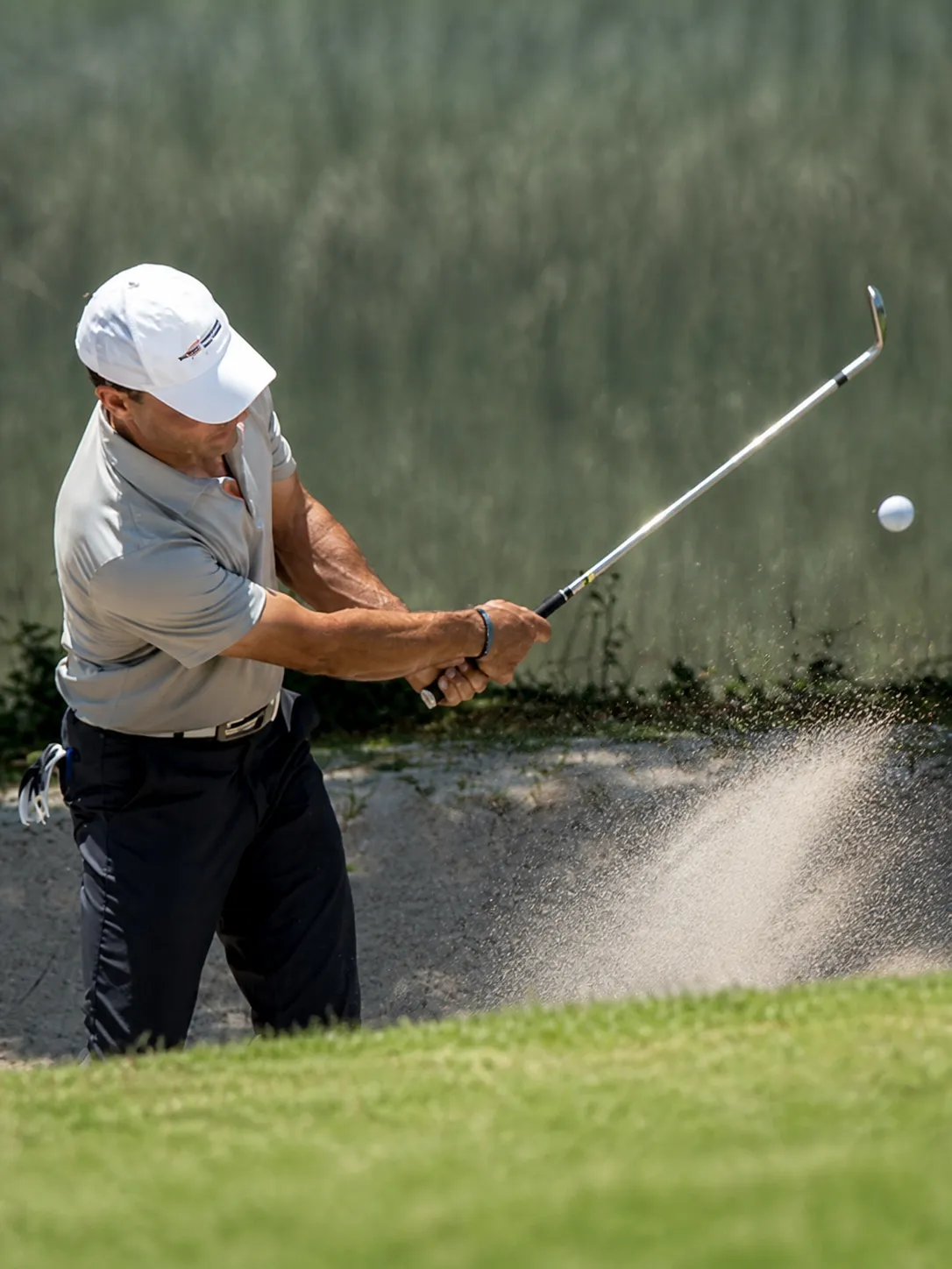 A golfer playing a shot out of a greenside bunker
